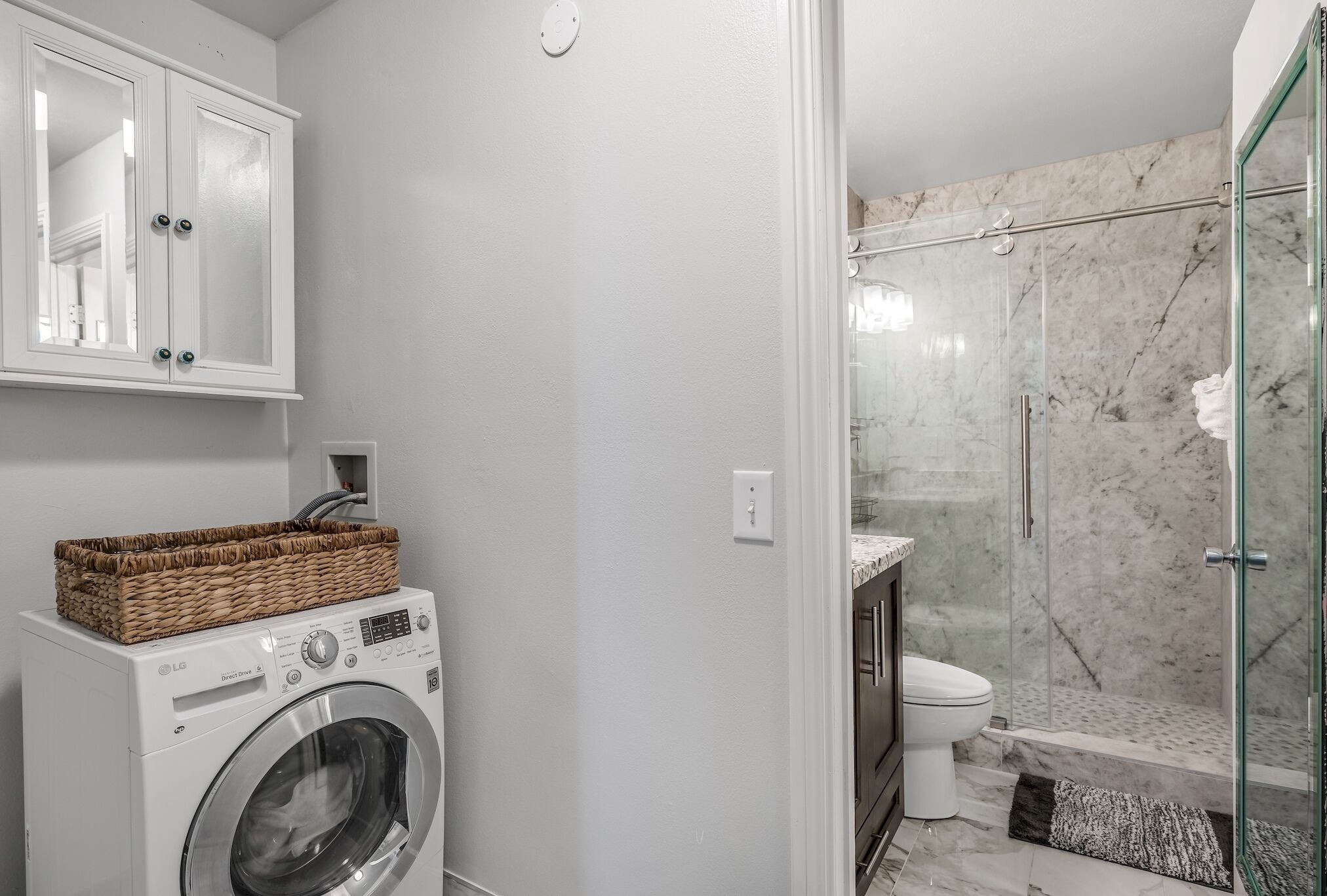 A compact bathroom with a washing machine, a glass shower enclosure, and a toilet.