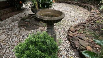 Un jardín con un bebedero de piedra para pájaros, un sendero de grava y diversas plantas.