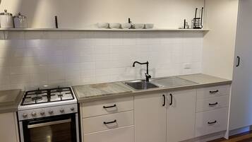 A kitchen with white cabinets, a stainless steel sink, a gas stove, and a wooden floor.