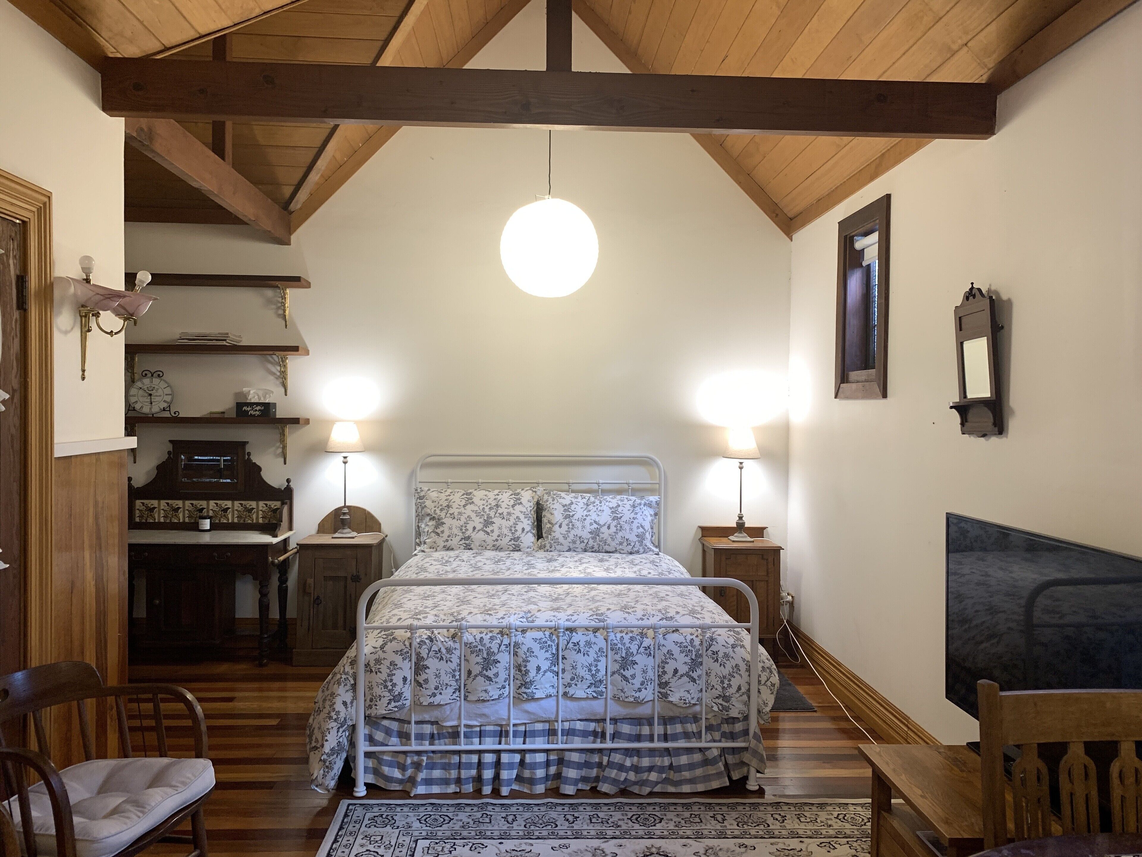 Una camera da letto con un letto, due abat-jour, un soffitto in legno, una sveglia e uno specchio a parete.