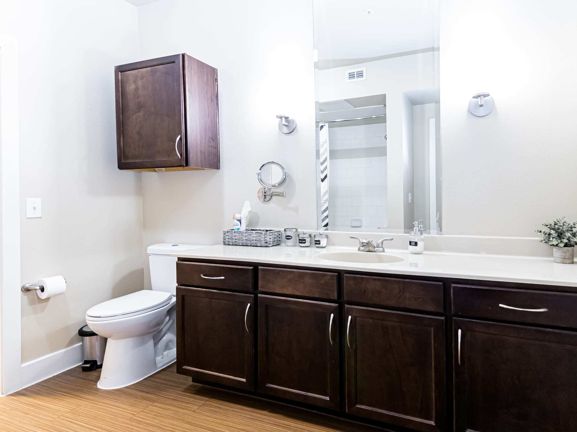 A modern bathroom with a toilet, sink, dark wooden cabinets, a mirror, and a small potted plant.