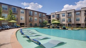 Une piscine entourée de bâtiments à plusieurs étages dotés de balcons, avec des chaises longues et des parasols à proximité.