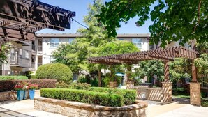 Une cour avec des jardinières en pierre, une pergola et un espace barbecue.