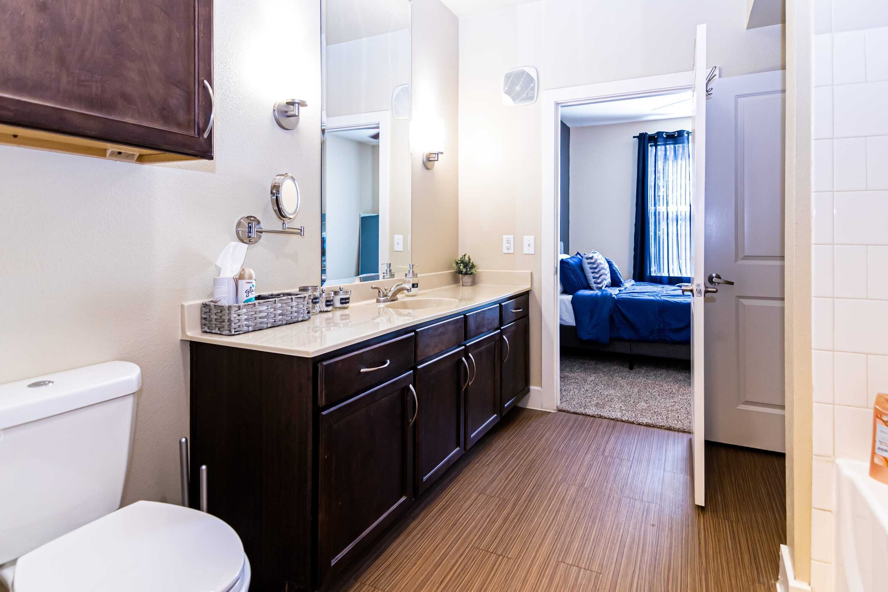 Un baño moderno con tocador de madera oscura, inodoro blanco y espejo grande.