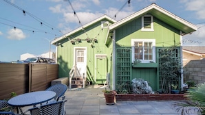 A green house with a patio, a small table, and chairs. - Across quiet street from sandy beach. (Sunset Beach)
