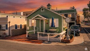 A small, green building with a porch and a clock, located on a street corner. - Across quiet street from sandy beach. (Sunset Beach)