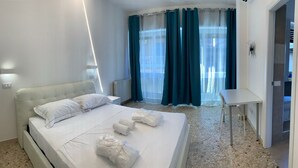 Een hotelkamer met een bed, een bureau en uitzicht buiten door dunne gordijnen.
