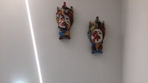 Een kamer met een witte nachtkastje, een wandlamp en twee decoratieve wanddecoraties.