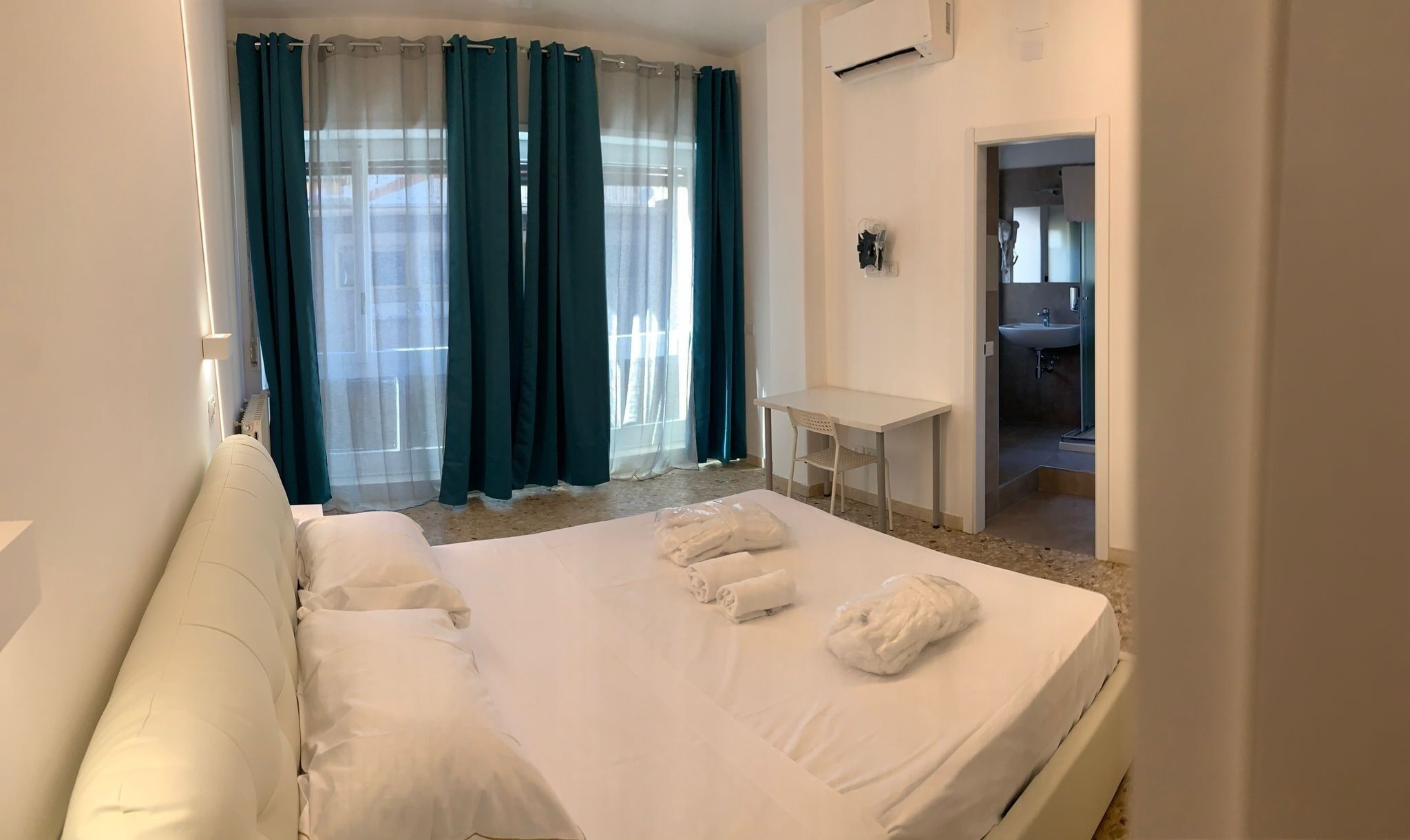 Une chambre d’hôtel avec un lit, un bureau et une salle de bain, visibles à travers une porte ouverte.