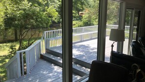 Vue depuis une pièce dotée de grandes fenêtres donnant sur une terrasse en bois et un lac, avec une lampe et une chaise visibles à l’intérieur.
