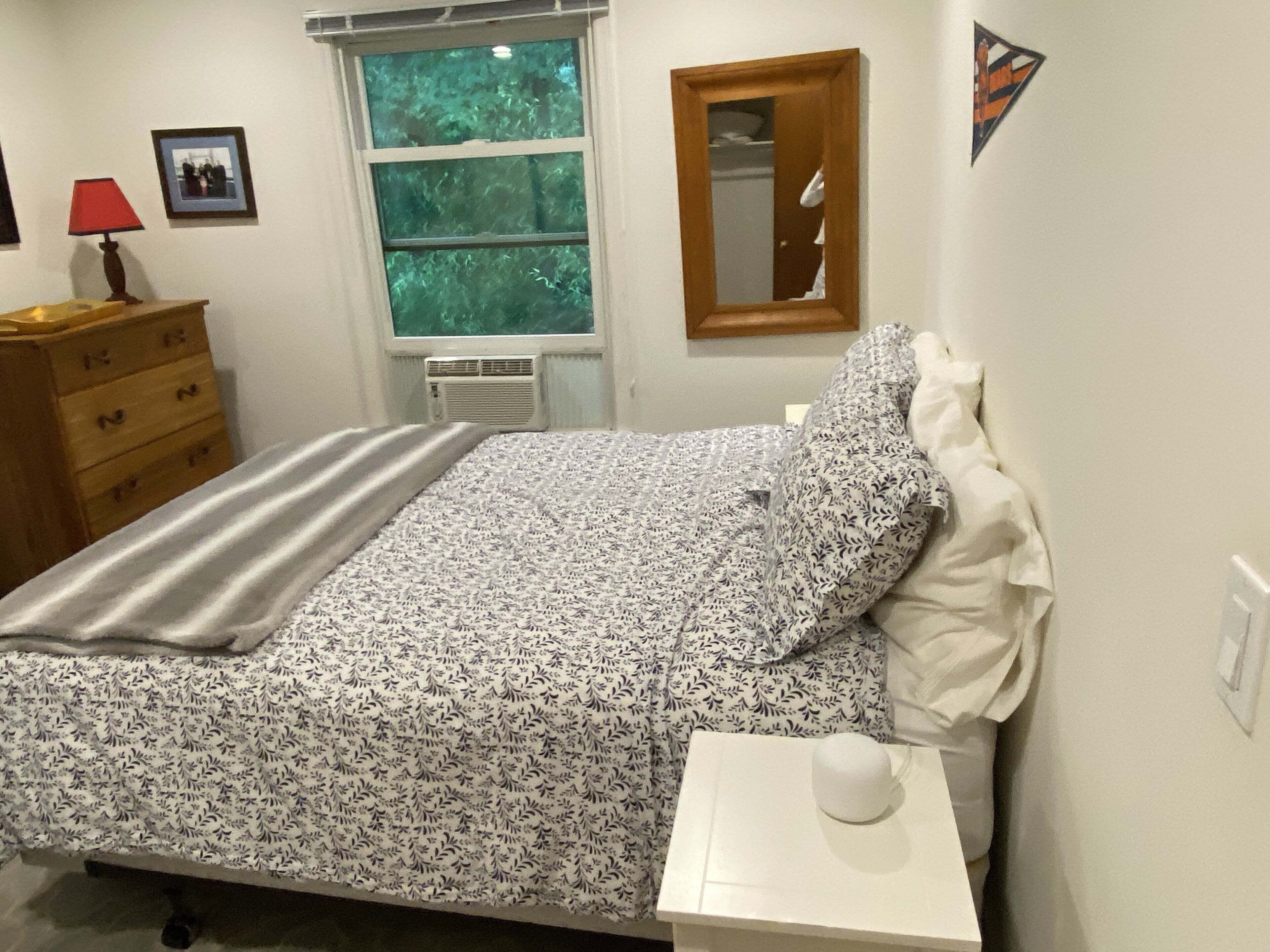 Ein Schlafzimmer mit Bett, Schminktisch, Fenster, Spiegel und Lampe.