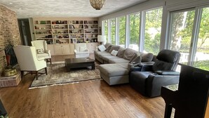Un salon spacieux avec un grand canapé d’angle, une table basse et une bibliothèque remplie de livres et d’objets de décoration.