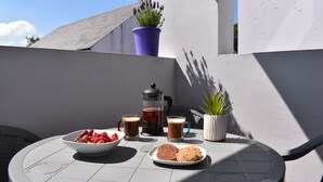 Een ronde tafel met een koffiezetapparaat, twee kopjes koffie, een schaal aardbeien en een bord koekjes op een balkon.