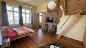 A room with a bed, a TV, a wooden staircase, and a window with curtains. - Bernsteinwohnung Gutshaus Reidervitz (Altenkirchen)