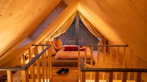 Una camera da letto mansardata accogliente, con soffitto spiovente, una scala in legno e un letto con cuscini e coperta.