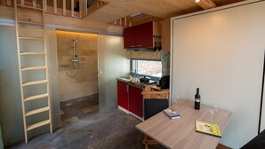 Una cucina compatta con soffitto in legno, un pensile rosso, un lavello e un tavolo da pranzo con una bottiglia di vino e bicchieri.