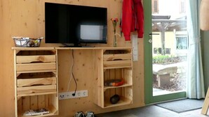 Un mobile in legno contenente una televisione, ripiani e una giacca rossa appesa al muro.