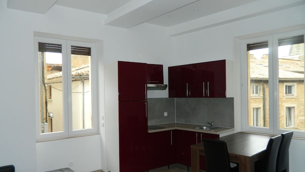 Eine kleine Küche mit Essbereich, mit einem roten Schrank, einer Spüle und einem Fenster mit Blick auf Gebäude.