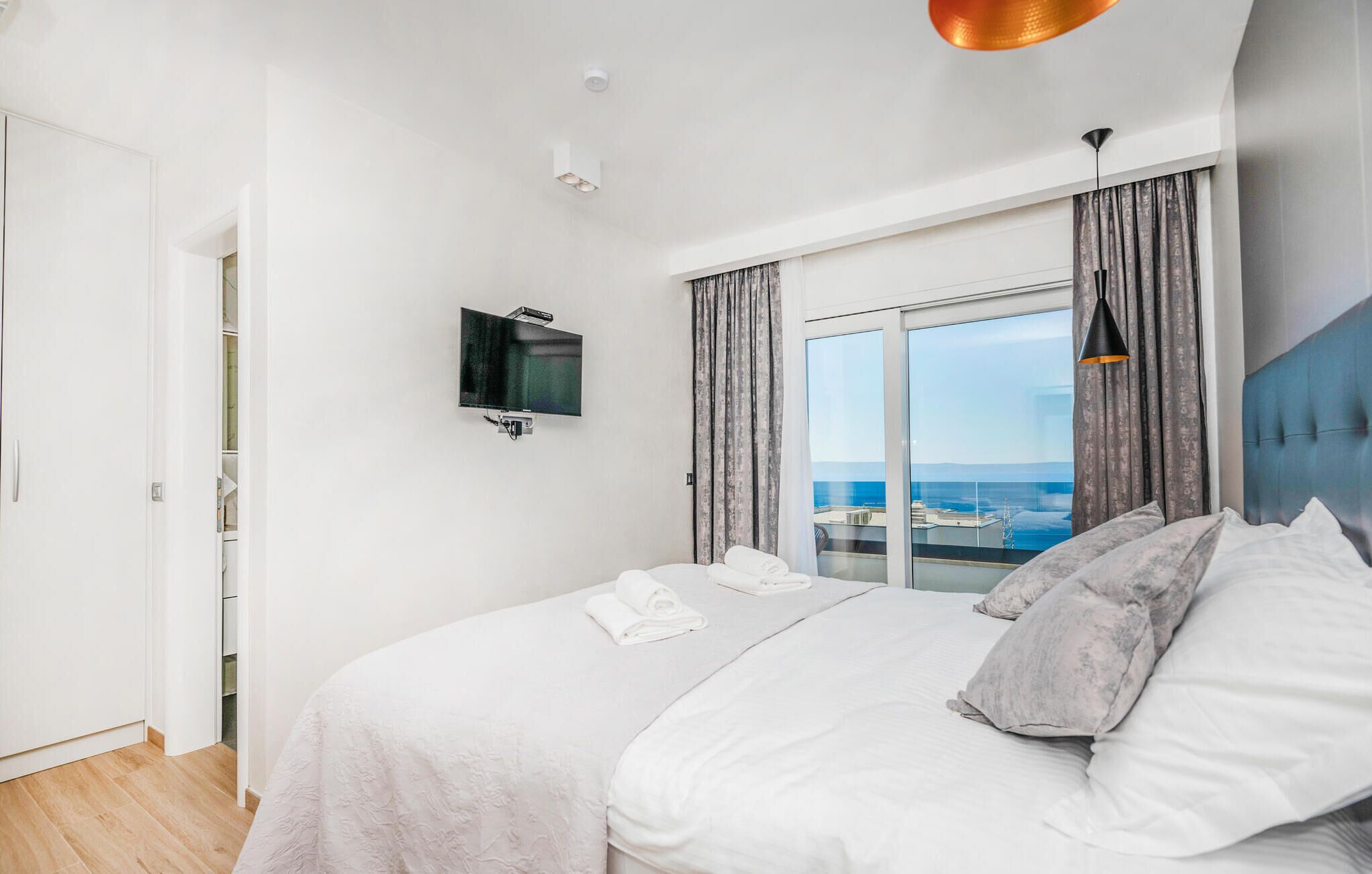 A hotel room with a bed, a television mounted on the wall, and a view of the sea through the window.