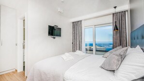 A hotel room with a bed, a television mounted on the wall, and a view of the sea through the window. - Gorgeous home in Makarska (Makarska)