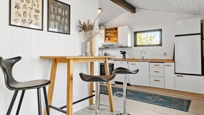 Ett modernt kök med vita köksskåp, ett matbord i trä, två barstolar och inramade botaniska illustrationer på väggen.