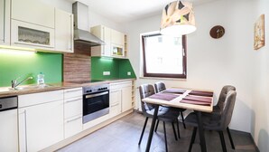 A modern kitchen with white cabinets, a green backsplash, and a dining area with a wooden table and chairs. - modernes Ferienhaus mit Garten (Techelsberg)