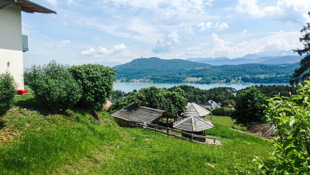 A rural landscape with a lake, mountains, and a white building with a red chair. - modernes Ferienhaus mit Garten (Techelsberg)