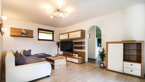 A modern living room with a sofa, TV, wooden shelves, and a small table. - modernes Ferienhaus mit Garten (Techelsberg)