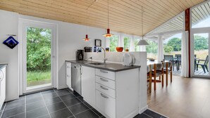 A modern kitchen with a large island, a dining area with outdoor seating, and a view of greenery. - 3 bedroom lovely home in Fanø (Fanø)