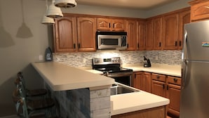 A kitchen with wooden cabinets, a stainless steel refrigerator, a microwave, a stove, and a granite island with a sink.