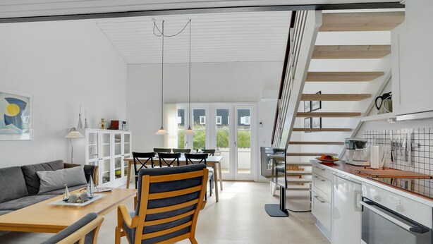 Uma cozinha moderna com forno Bosch, área de refeições com mesa e cadeiras de madeira, e escada que dá acesso a um andar superior.