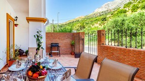 Un área de comedor al aire libre con una mesa preparada para dos, una silla, una mesita y una planta en maceta.