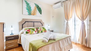 Un dormitorio ordenado con cama, mesitas de noche, aire acondicionado de pared y ventana con cortinas.