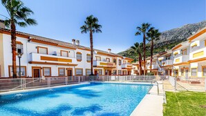 Una piscina rodeada de edificios de varios pisos con balcones, palmeras y un telón de fondo montañoso.