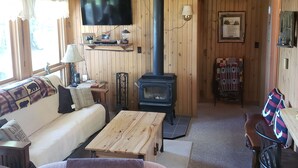 Ein gemütliches Blockhaus-Interieur mit Holzbalkendecke, Kamin, Sofa, Couchtisch und einem an der Wand befestigten Fernseher.