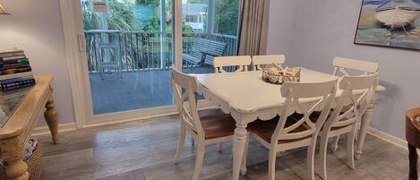 A dining area with a white table and chairs, a hanging light fixture, and a view of the outdoors through a glass door.