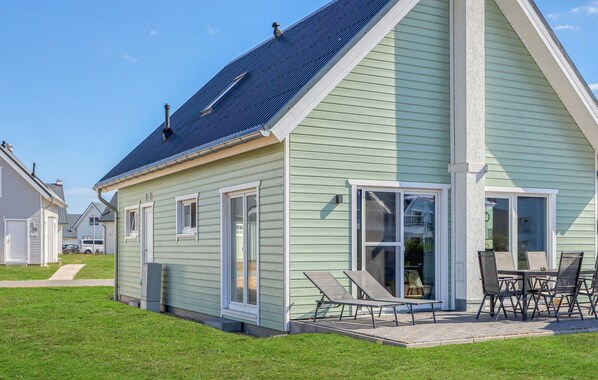 A single-story house with a sloped roof, large windows, and a patio area with outdoor furniture. - Cozy home in OstseeResort Olpenitz with sauna (OstseeResort Olpenitz)