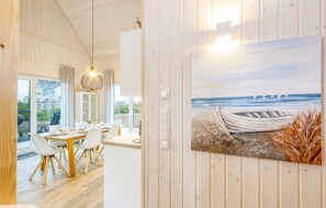 A dining area with a wooden table and chairs, a cabinet, and a painting of a boat on a beach. - Cozy home in OstseeResort Olpenitz with sauna (OstseeResort Olpenitz)