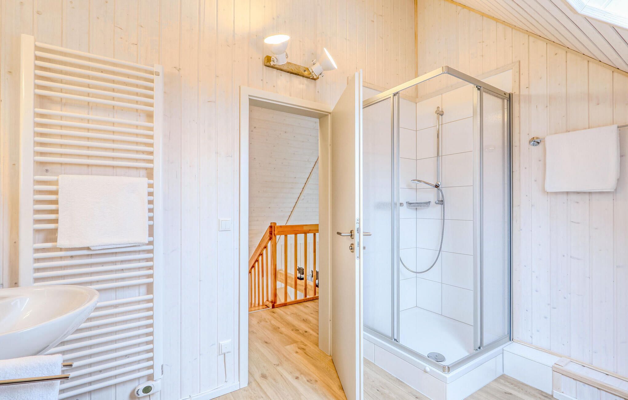 A modern bathroom with a glass-enclosed shower, wooden flooring, and a white sink.