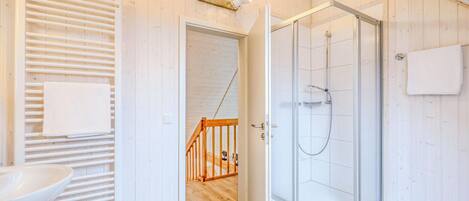 A modern bathroom with a glass-enclosed shower, wooden flooring, and a white sink.