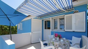 A patio with a table set for two, white chairs, and a striped awning providing shade.