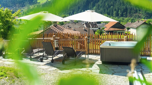 A patio area with outdoor furniture, a hot tub, and a wooden fence. - Zirm Apartment - with open air jacuzzi & infrared sauna! (Sankt Sigmund)