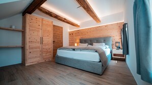 A bedroom with a large bed, wooden wardrobe, and a nightstand. - Zirm Apartment - with open air jacuzzi & infrared sauna! (Sankt Sigmund)