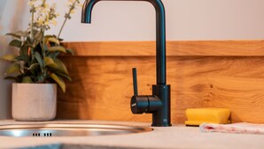 A modern kitchen with a black faucet, wooden shelves, and a potted plant. - Zirm Apartment - with open air jacuzzi & infrared sauna! (Sankt Sigmund)