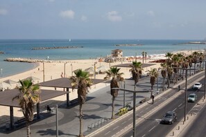 A coastal road with a beach, palm trees, and a clear sky. - Panoramic Seaview Balcony Escape (Tel Aviv-Yafo)