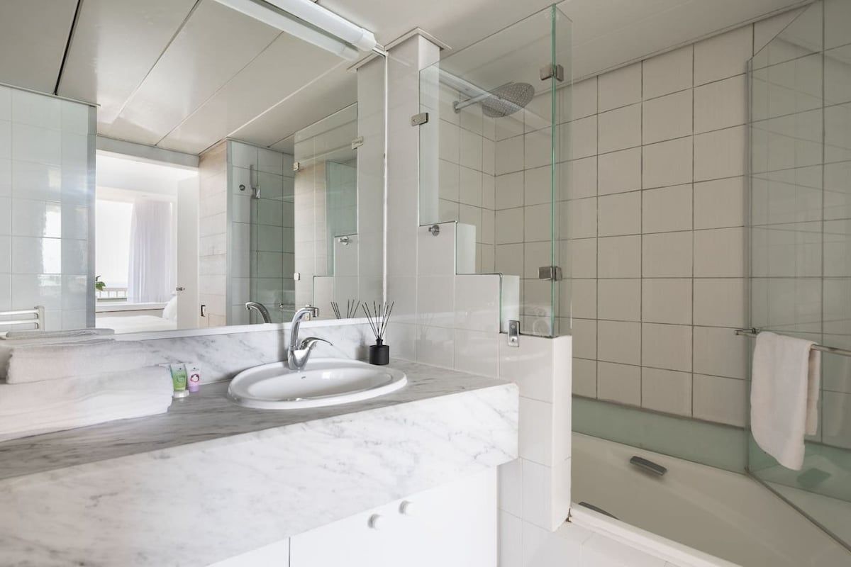 A modern bathroom with a glass shower enclosure, a marble sink, and a large mirror.