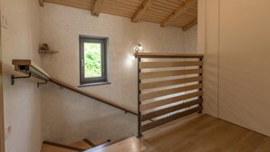 A staircase with a wooden handrail and a small window with a view of greenery.