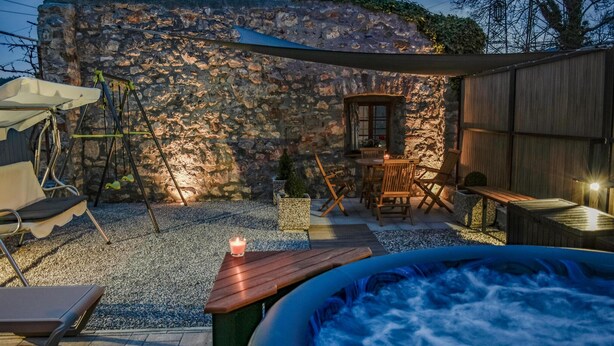 A hot tub with a stone wall backdrop, outdoor seating, and a small table with a candle.