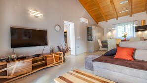 A modern living room with a flat-screen TV, wooden entertainment unit, and a sofa with orange pillows.