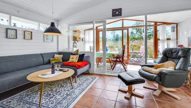 Een moderne woonkamer met een grijze bank, een zwarte lederen fauteuil, een ronde salontafel en een groot raam met uitzicht op de omgeving.